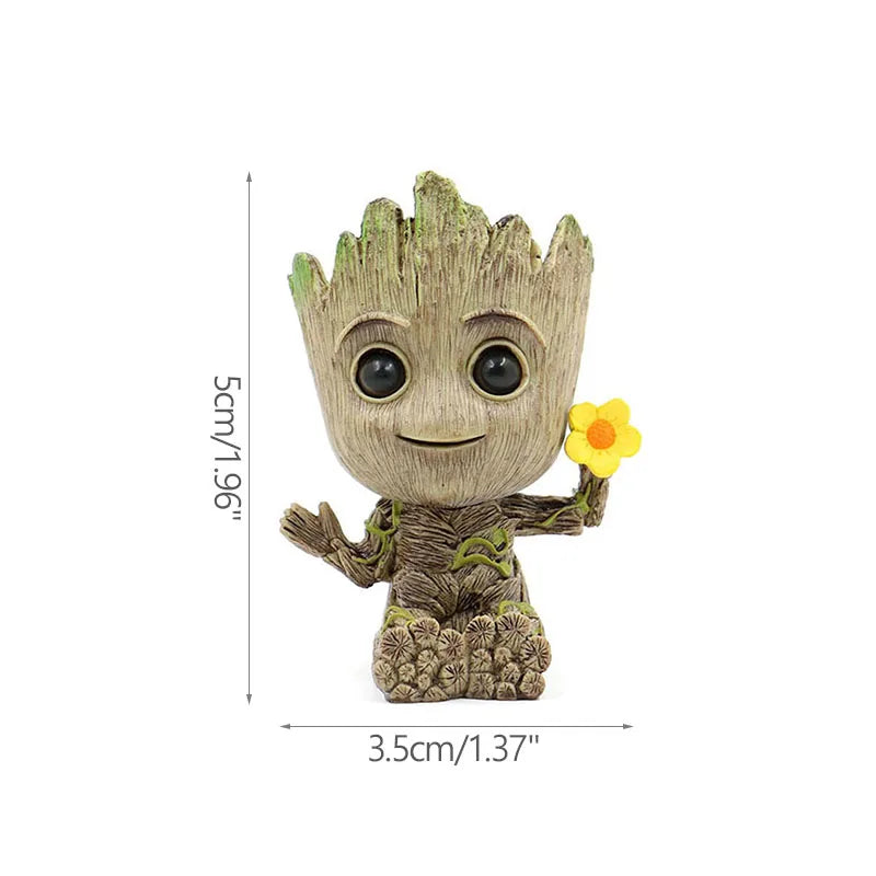 Figura pequeña de adorno en forma de tronco sonriente, sostiene flor amarilla, medidas visibles.