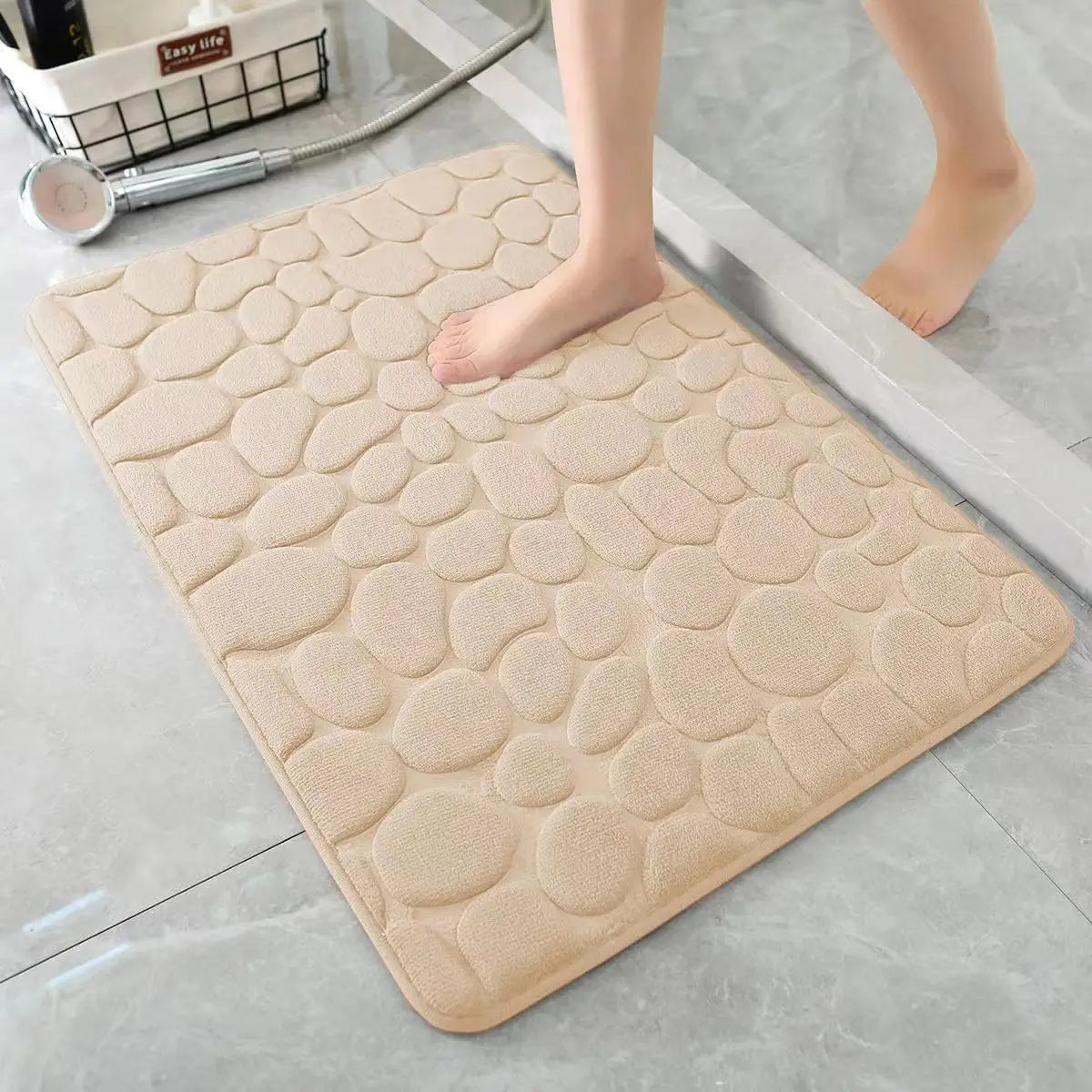 Alfombra de baño antideslizante beige con textura de piedras sobre suelo de cerámica, uso en hogar moderno.