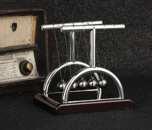 Péndulo de Newton metálico decorativo sobre mesa oscura junto a radio vintage, accesorio moderno para hogar.