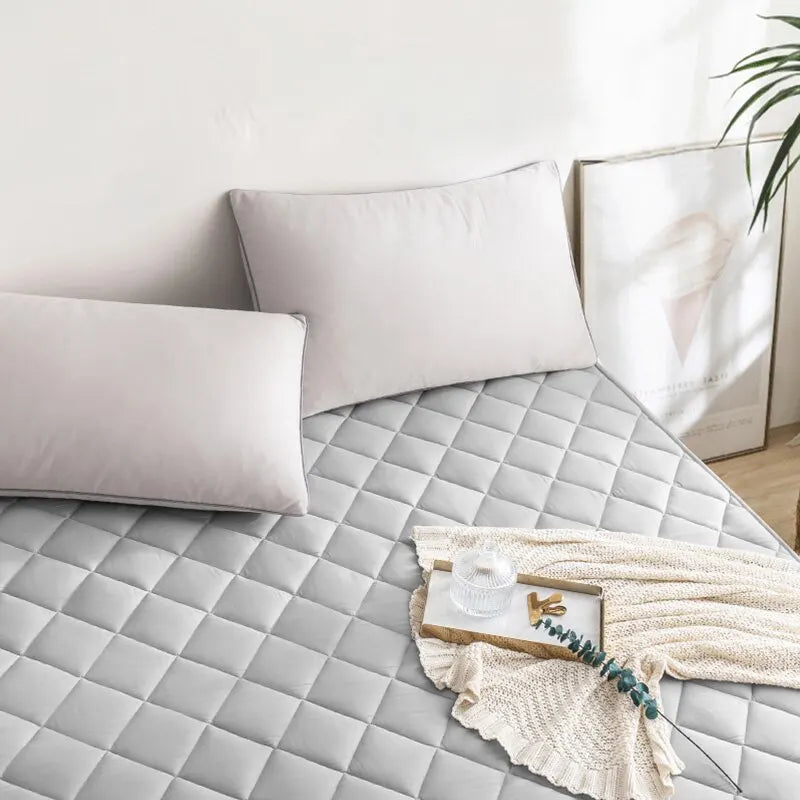Colchón gris acolchado en cama moderna con cojines, manta y bandeja decorativa, dormitorio luminoso