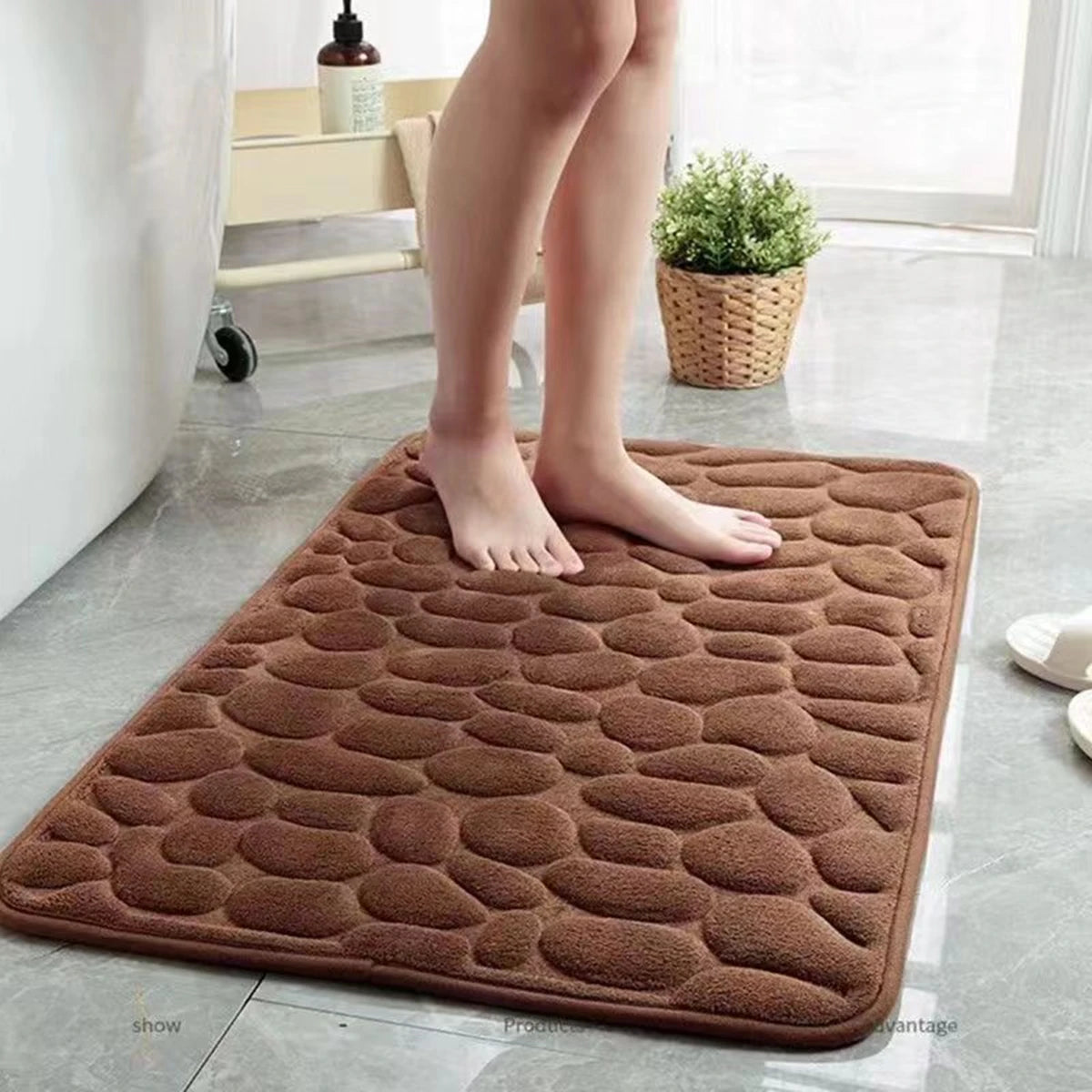 alfombra marrón antideslizante para baño con diseño de piedras y pies descalzos sobre suelo gris