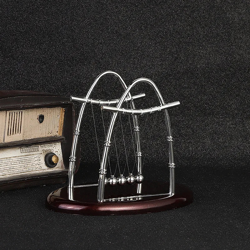 Péndulo de Newton decorativo plateado sobre base marrón, junto a radio retro, fondo negro.