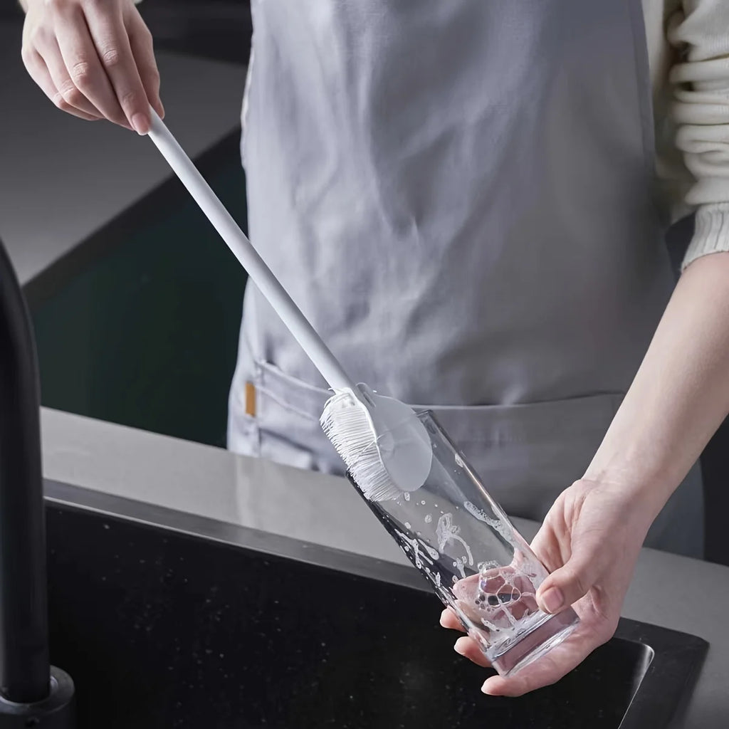 Persona limpiando un vaso de cristal con cepillo largo en fregadero de cocina moderna